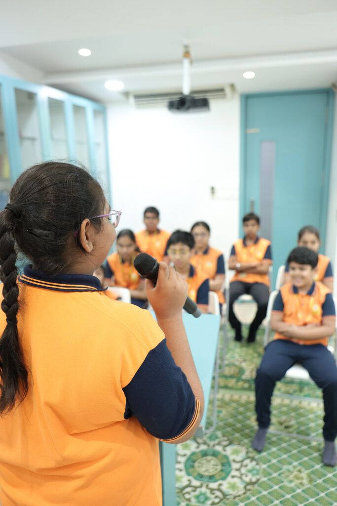 A student confidently delivering a speech addressing a classroom filled with students